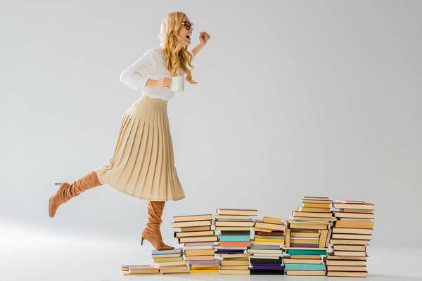 adult stylish woman standing on books with white mug 