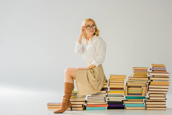 beautiful blonde woman in glasses sitting on pile of retro books