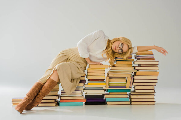 tired blonde woman in glasses laying on pile of retro books