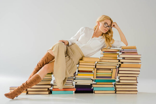 beautiful blonde woman in glasses laying on pile of retro books