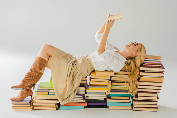 beautiful blonde woman in glasses reading and laying on pile of retro books