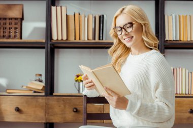 güzel kadının içinde oturan ve oturma odasında kitap okuma gözlük yakın çekim