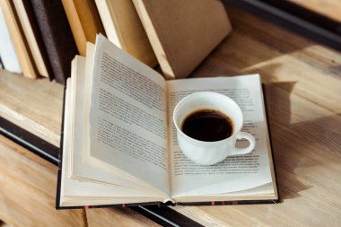 close up of open book with cup of coffee on bookshelf clipart
