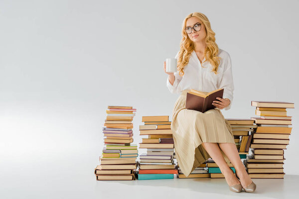 beautiful adult woman sitting on pile of retro books with white cup