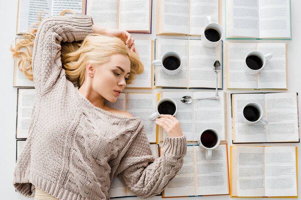 woman laying near clock made of white cups with coffee and spoons on open books