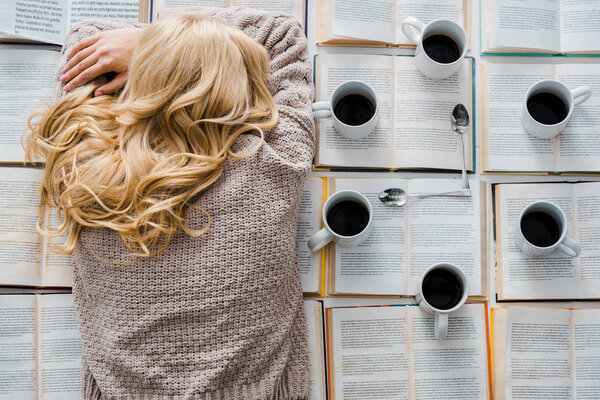 усталая женщина спит возле часов, сделанных из белых чашек с кофе и ложек на открытых книгах
