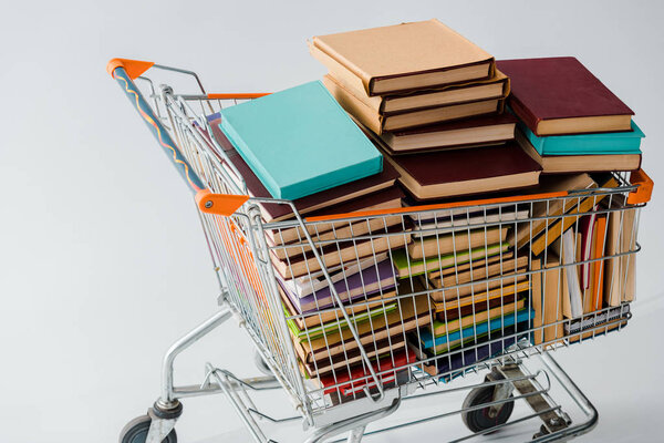 pile of vintage books with multicolored covers in shopping cart isolated on grey