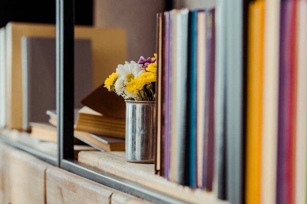 close up of bookshelf  with flowers in can and books
