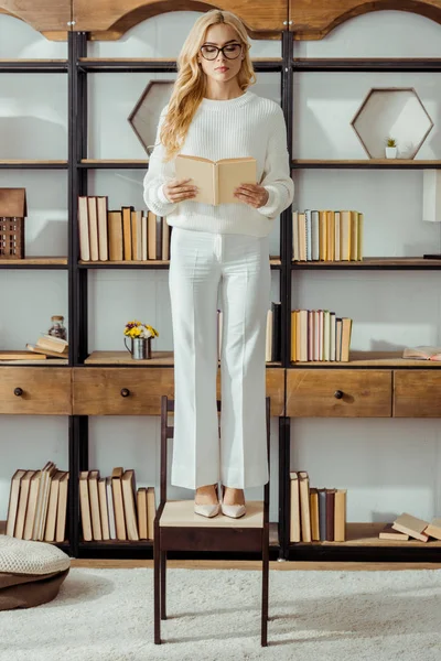 Erwachsene Frau Mit Brille Steht Auf Stuhl Wohnzimmer Und Liest — Stockfoto