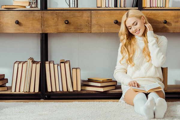 улыбающаяся женщина, сидящая на полу и читающая книгу в гостиной
