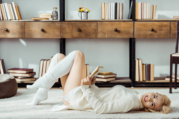 smiling beautiful woman laying on carpet and reading book