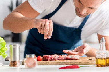 close up of handsome man salting steak on cutting board clipart