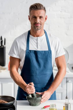 handsome man crushing spices on kitchen table clipart
