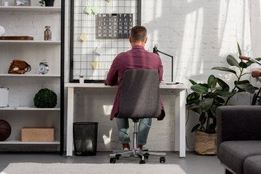 back view of man sitting on chair and working at home office clipart