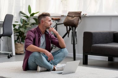 thoughtful man sitting on floor in home office with laptop