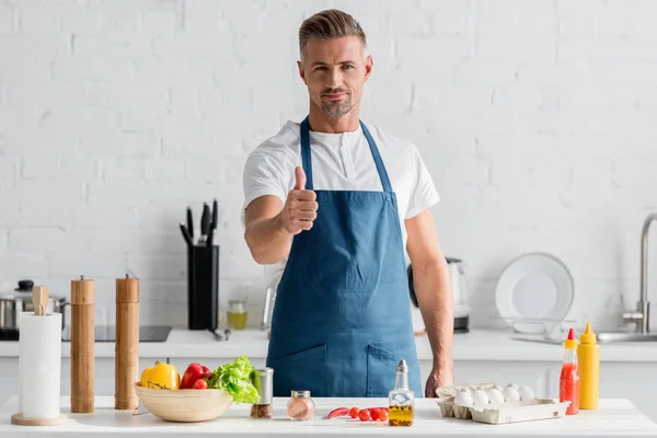 男子在围裙站在厨房 并显示竖起大拇指的标志 — 图库照片