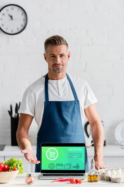 英俊的成年男子站在笔记本电脑屏幕上的笔记本电脑屏幕上的厨房桌子上的网上购物插图 — 图库照片