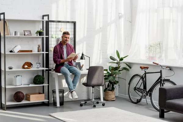 Schöner Mann Sitzt Auf Dem Tisch Und Liest Buch Hause — Stockfoto