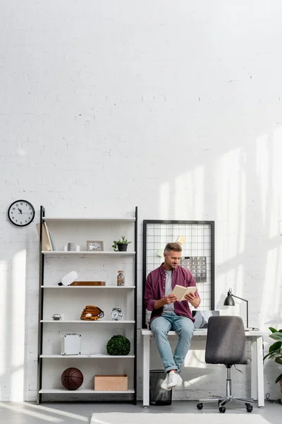 Sorrindo Homem Sentado Mesa Lendo Livro Casa Escritório — Fotografia de Stock