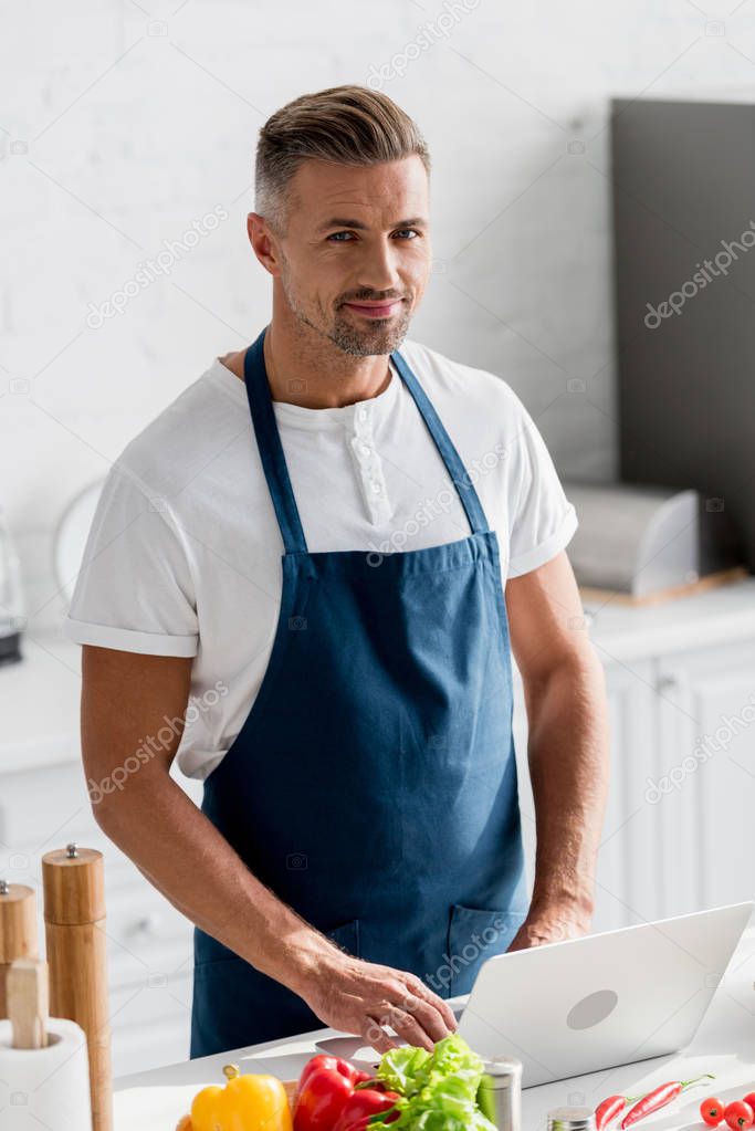 handsome man standing at kitchen and working on laptop 
