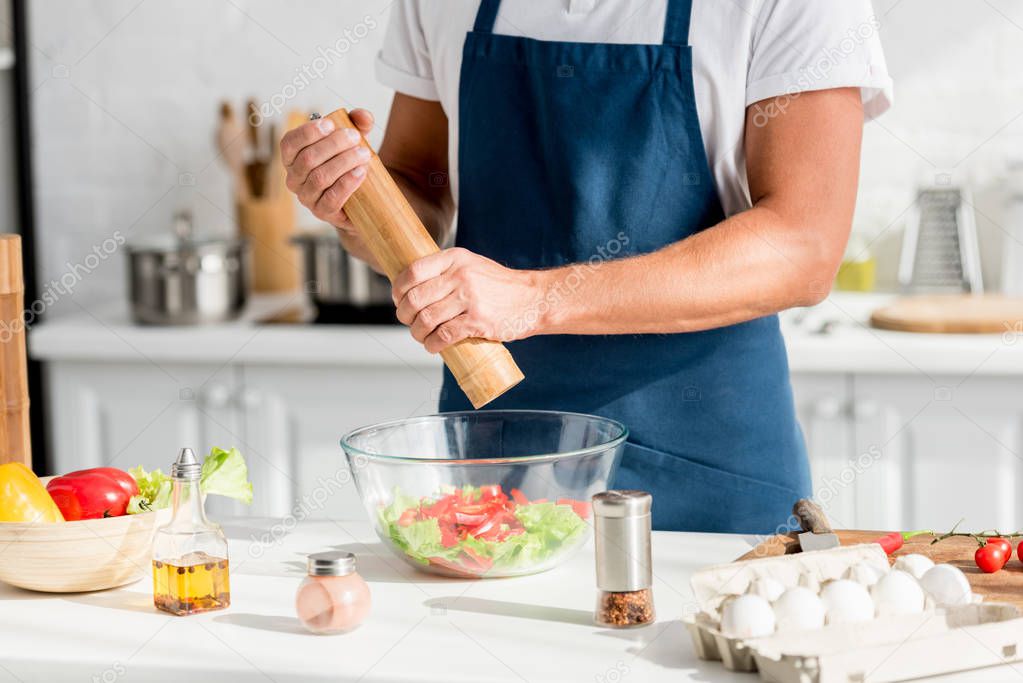 partial view of man in apron salting salad at kitchen