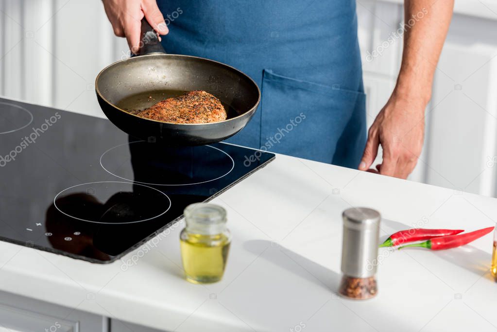 partial view of man roasting steak on stove