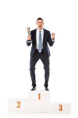 excited emotional businessman with trophy cup standing on winners podium isolated on white