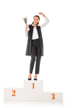 excited business winner holding trophy cup while standing on winners podium isolated on white clipart