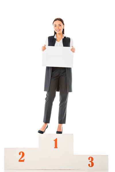 attractive businesswoman with empty board standing on winners podium isolated on white