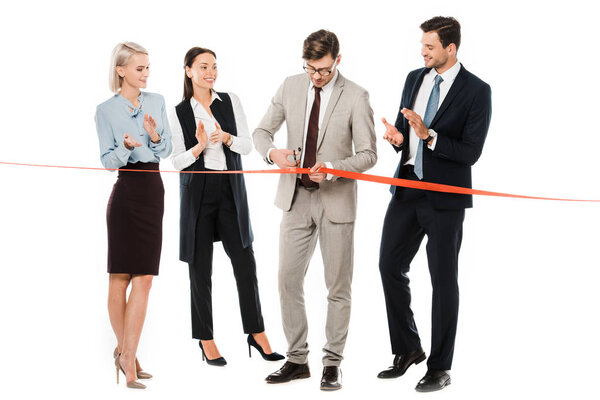 businessman cutting red ribbon on opening ceremony while colleagues applauding, isolated on white