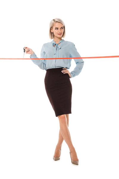 beautiful smiling businesswoman standing with scissors near red ceremonial ribbon for grand opening, isolated on white