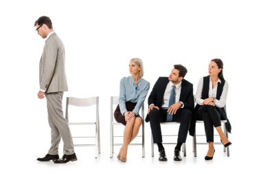 fired businessman going away while colleagues sitting on chairs and looking at him isolated on white clipart
