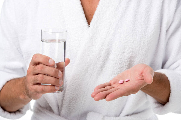 cropped image of adult man in bathrobe holding pills and glass of water isolated on white