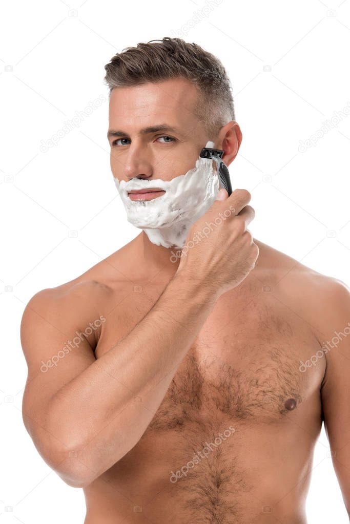 muscular shirtless man with foam on face shaving with razor isolated on white