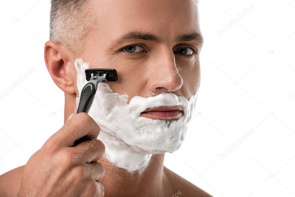 close up portrait of man with foam on face shaving with razor isolated on white