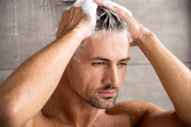 close up portrait of adult man washing hair with shampoo and taking shower  clipart