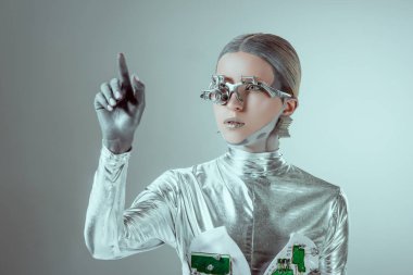 futuristic silver cyborg gesturing with hand and looking away isolated on grey, future technology concept  
