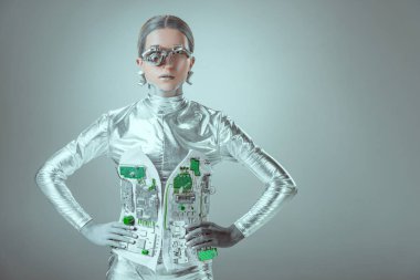 futuristic silver cyborg standing with hands on waist and looking at camera isolated on grey, future technology concept  clipart