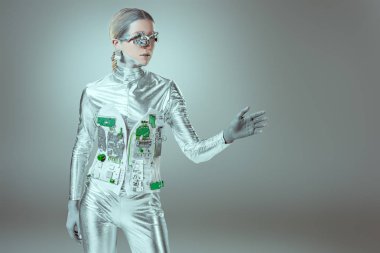silver woman robot gesturing with hand and looking away on grey, future technology concept  clipart