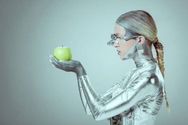holding ve yeşil elma izole gri, geleceğin teknoloji kavramı üzerinde inceleyerek cyborg yan görünüm 