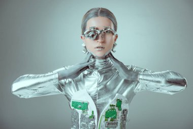 Genç kadın robot boyun dokunmadan ve izole gri, geleceğin teknoloji kavramı üzerinde kamera bakıyor 
