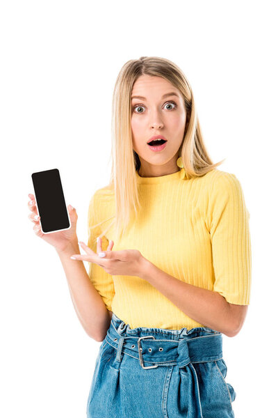 shocked young woman showing smartphone with blank screen and looking at camera isolated on white