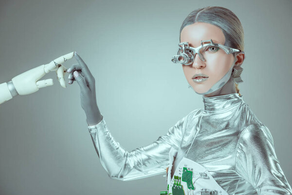 cyborg touching robotic arm and looking at camera isolated on grey, future technology concept