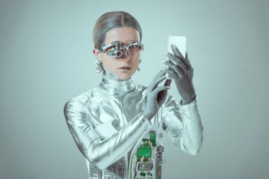 young woman robot using smartphone isolated on grey, future technology concept