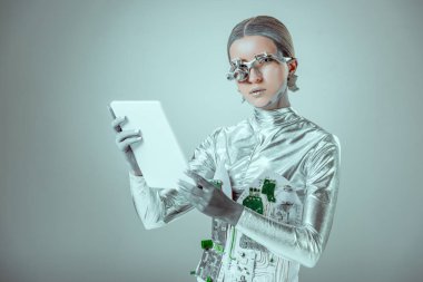 Gümüş robot tablet holding ve izole gri, geleceğin teknoloji kavramı üzerinde kamera bakıyor