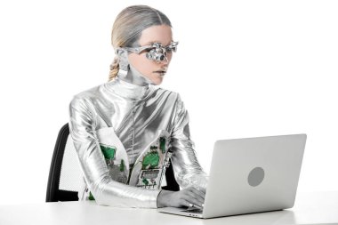 Gümüş robot masada oturan ve izole beyaz, geleceğin teknoloji kavramı üzerinde dizüstü bilgisayar ile çalışma