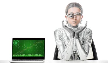 Gümüş robot izole beyaz, geleceğin teknoloji kavramı üzerinde grafik cihazı ile dizüstü yakınındaki masada oturan