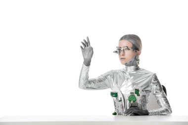 masada oturan ve izole beyaz, geleceğin teknoloji kavramı üzerinde bir şey dokunmak göz protez ile gümüş robot 