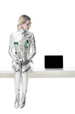 Gümüş robot izole beyaz, geleceğin teknoloji kavramı üzerinde boş ekran ile dizüstü yakınındaki masada oturan