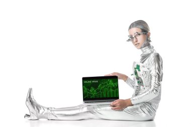 oturma ve izole beyaz, geleceğin teknoloji kavramı üzerinde online ticaret cihazı ile dizüstü bilgisayarı gösteren gümüş robot
